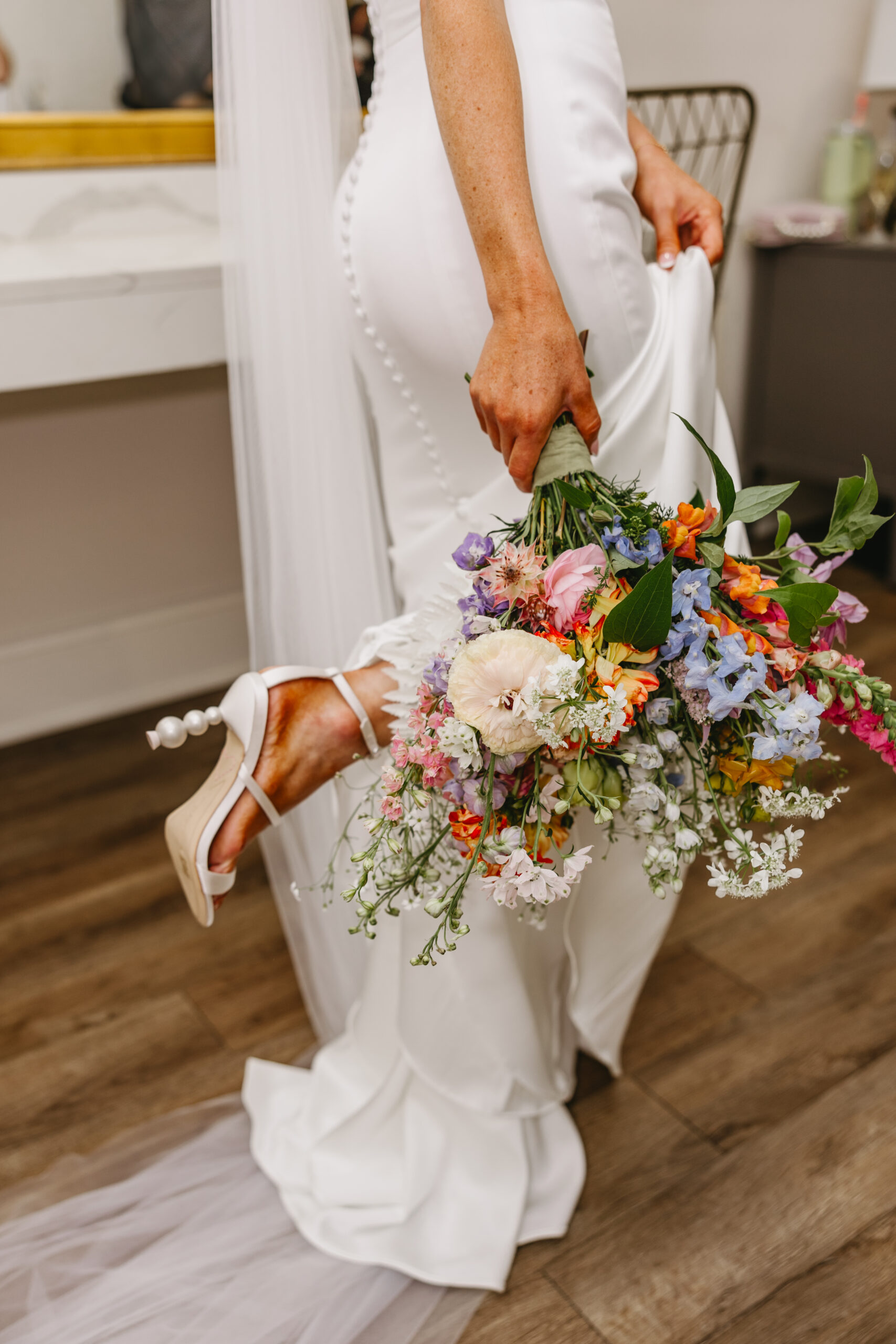 A bride getting ready for her wedding holding her bouquet and showing off her heels.