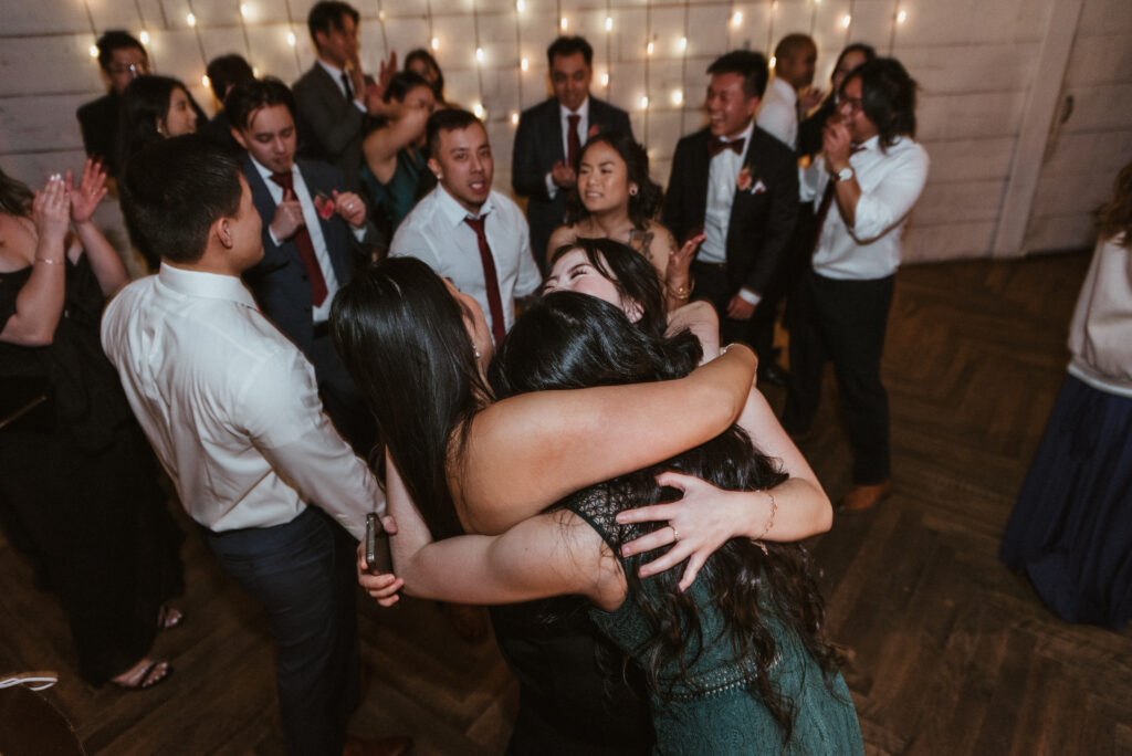 Friends in a group hug on a dance floor at a wedding reception at Terrain at Styers in Glen Mills, Pa.