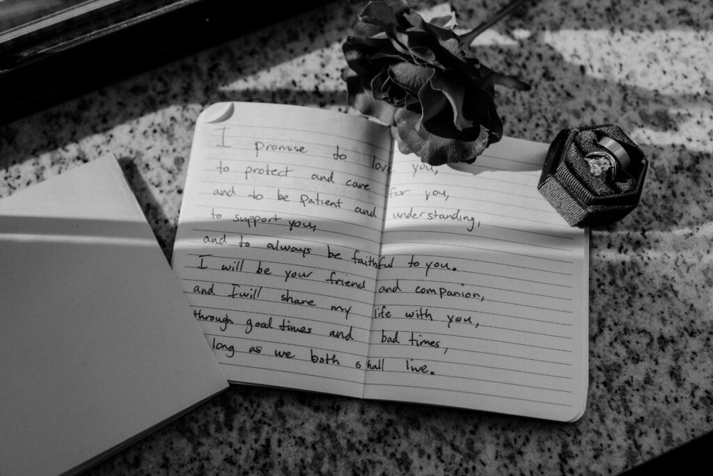 Picture of a couples open wedding vow book with their wedding bands on a window sill. 