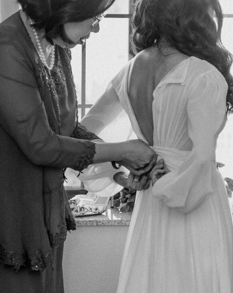 A mother helping her daughter zip up her wedding dress.