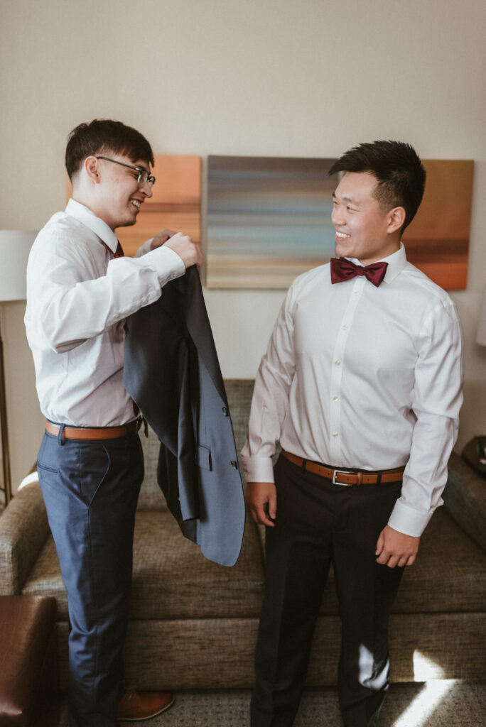 A best man helping a groom put on his suit jacket.