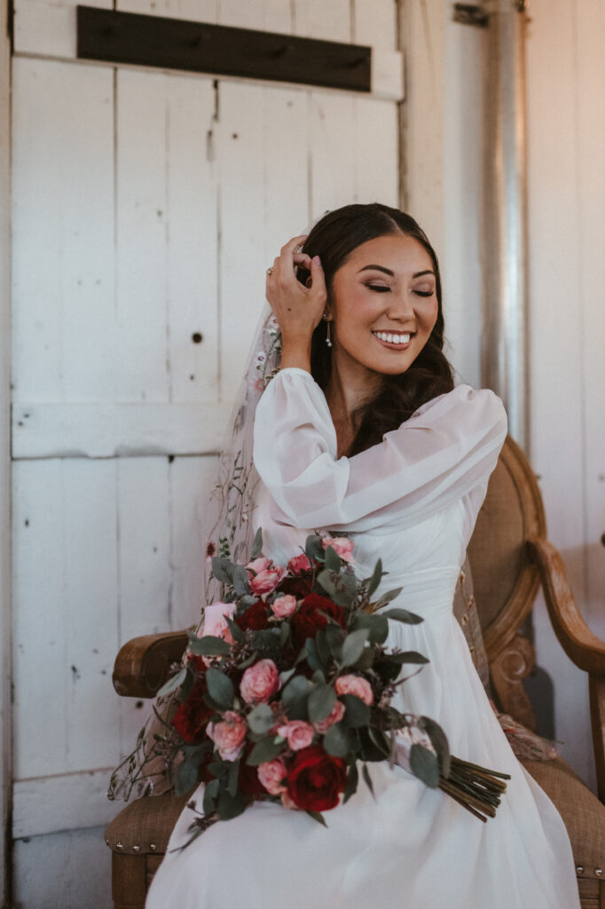 A bride posing in a chair her wedding dress, veil, and bouquet.