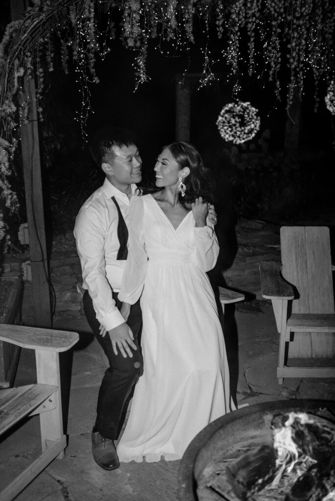 A bride and groom sit out by a fire during their wedding reception.