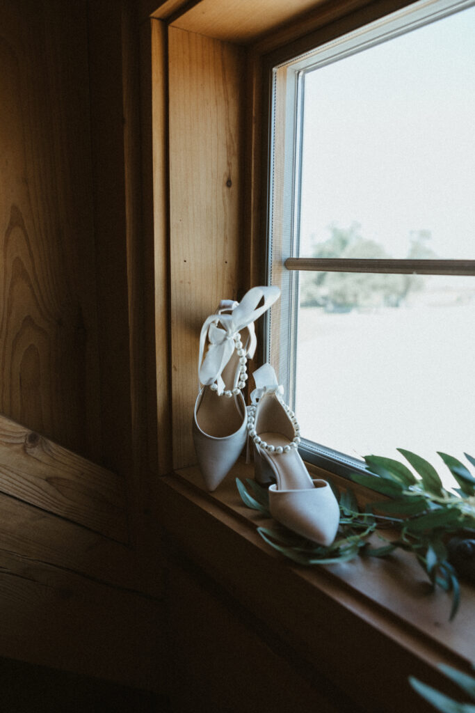 White wedding heels with pearl detailing around ankle propped in a window sill. 