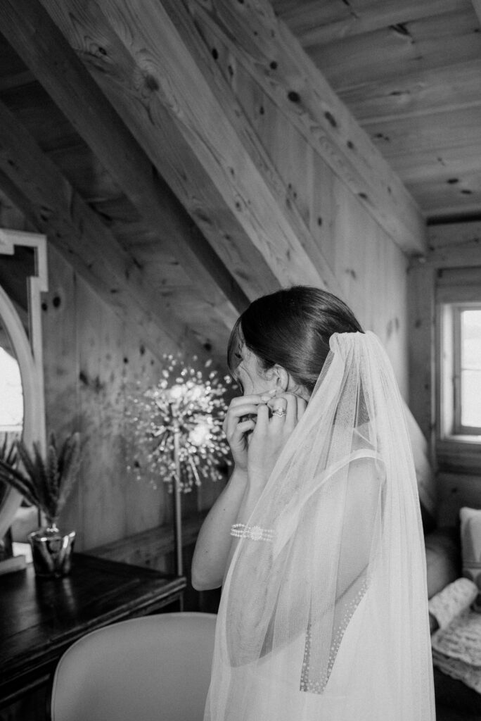 Bride looking in the mirror as she puts her earings in with her veil drapped over her shoulder.