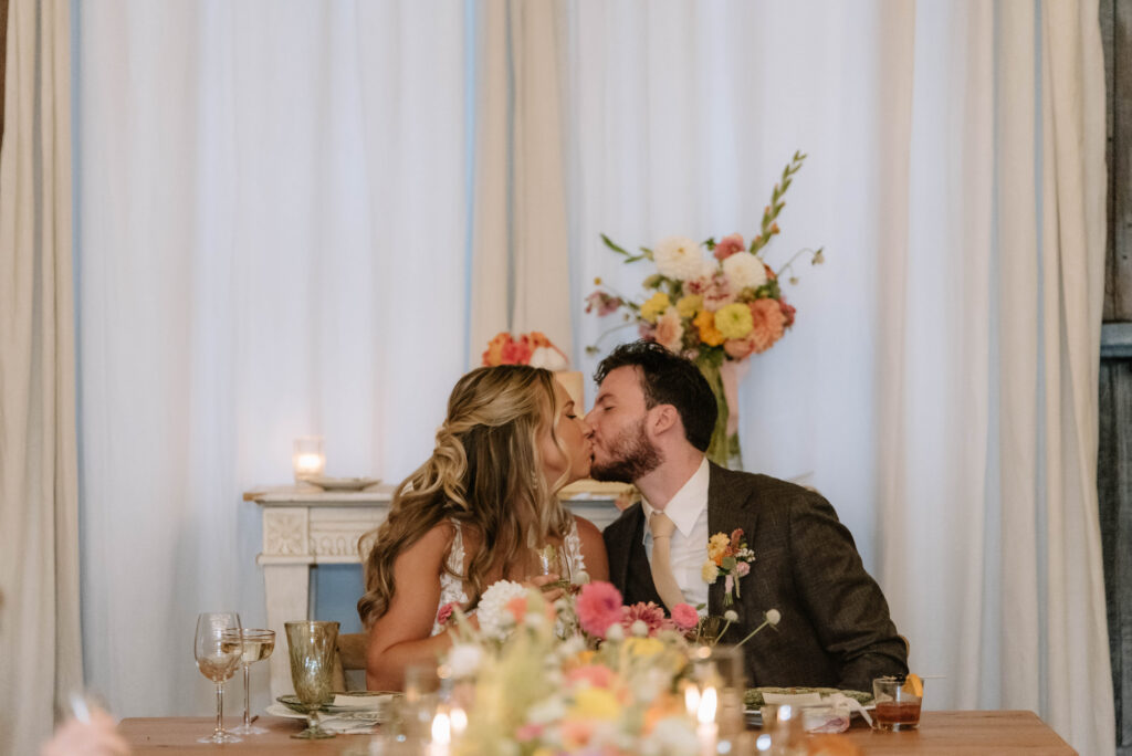 Bride and groom kiss after toasts at their head table at their wedding reception at Terrain Gardens at Styers in Glen Mills, PA!