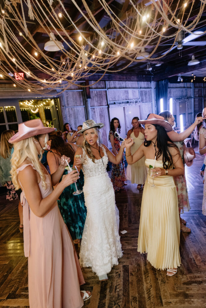 Bride and friends dance with cowboy hats and glasses at their wedding reception at Terrain Gardens at Styers in Glen Mills, PA!