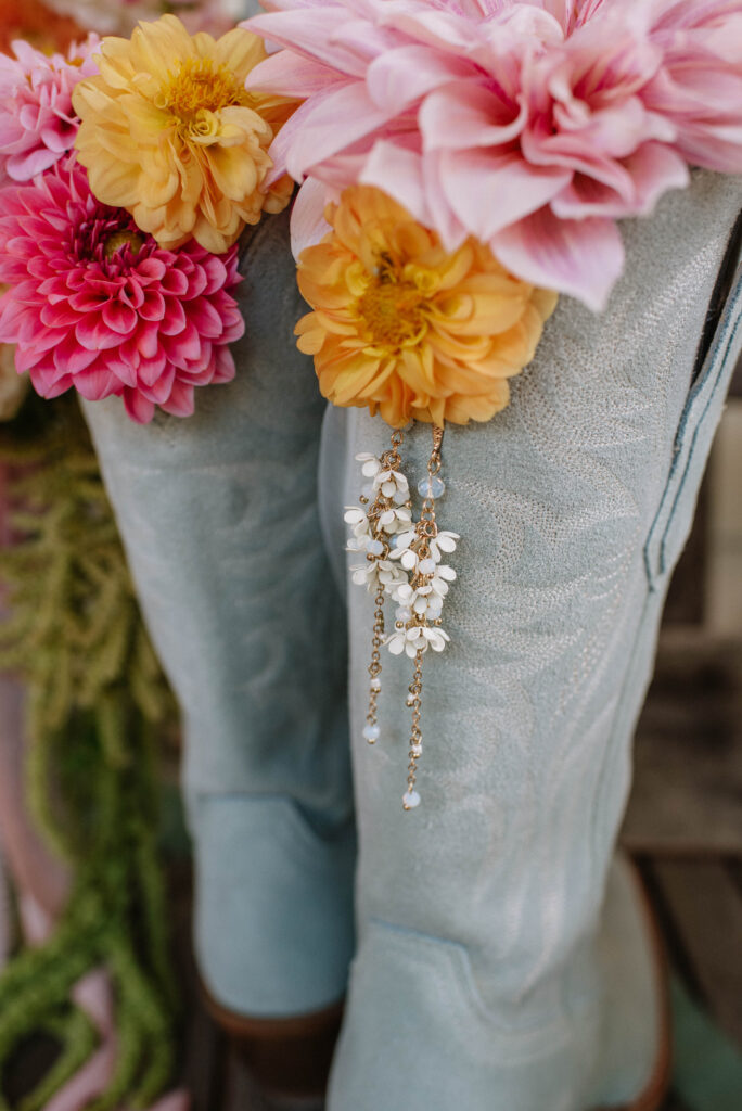 Blue cowboy boots with wildflowers and earrings hanging from them. 