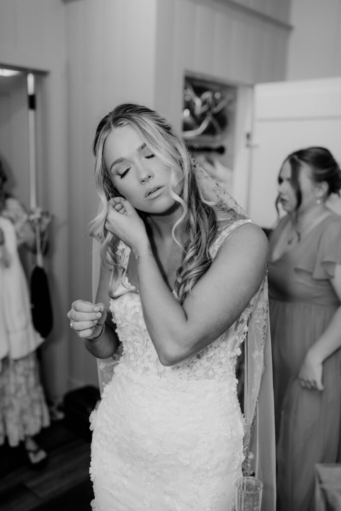 Bride putting on her earrings in black and white.