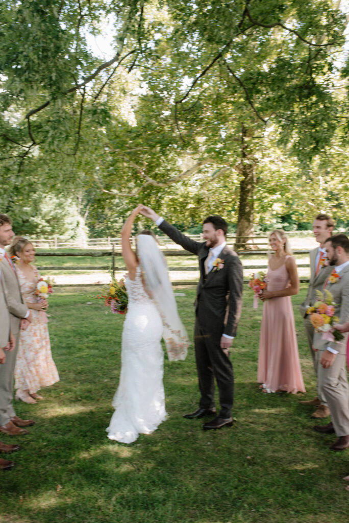 Groom spinning his bride while their wedding party watches with dramatic blur. Documentary vibes at Inn at Grace Winery in Glen Mills, PA.