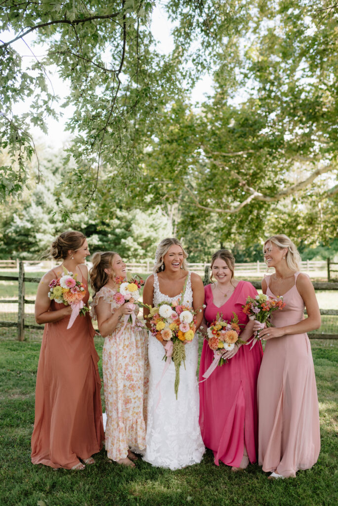 Bride and her bridesmaids in assorted pink and floral dresses with wildflower bouquets at the Inn at Grace Winery in Glen Mills, PA. 