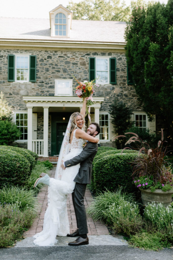 Groom picking his bride up in celebration at the Inn at Grace Winery in Glen Mills, PA.   Documentary style wedding photography, Philadelphia, PA.