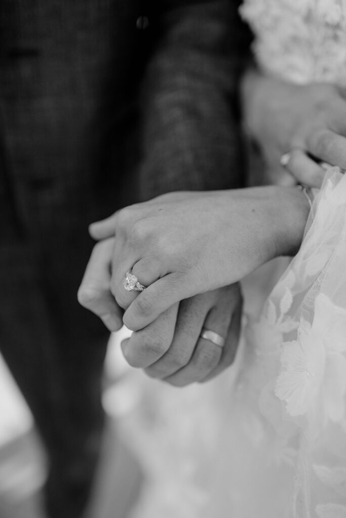 Bride and groom holding hands and showing their wedding ring details in black and white at Terrain Gardens at Styers in Glen Mills, PA. 