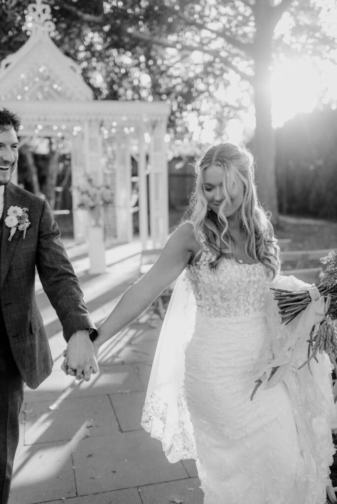 Documentary style wedding photography of bride and groom walking hand in hand in black and white at Terrain Gardens at Styers in Glen Mills, PA. 