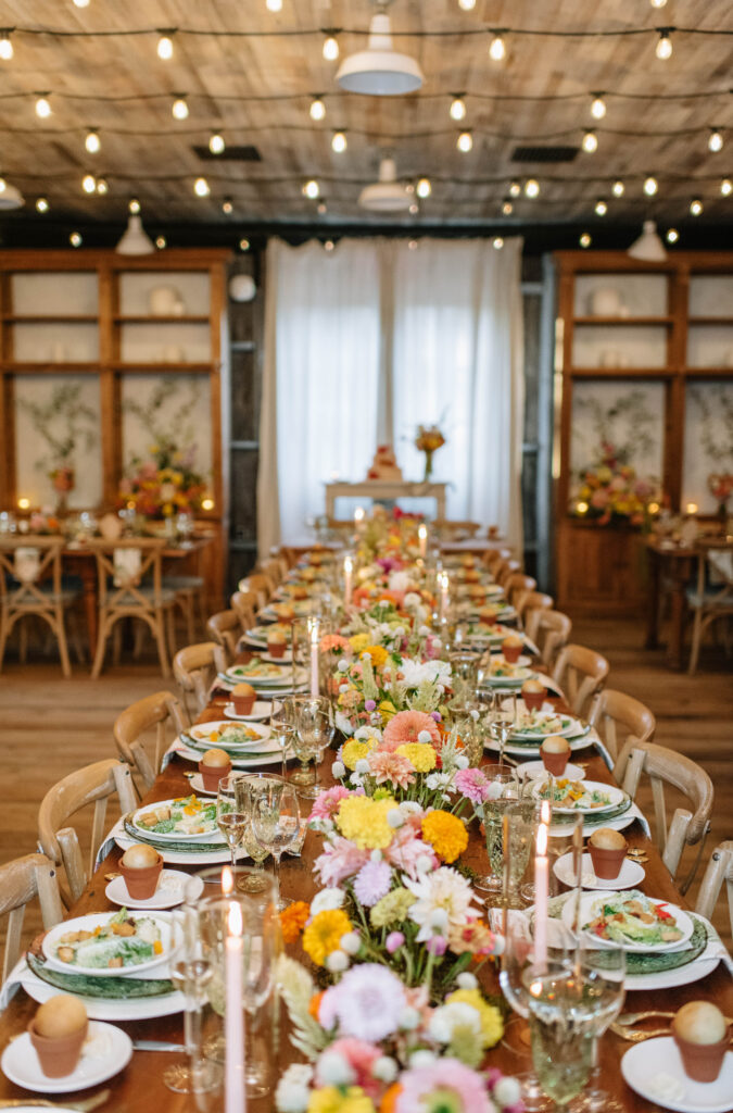Stunning wedding reception details of colorful wildflower details, candles, green glass plates, wood chairs, ornate cups at Terrain Gardens at Styers in Glen Mills, PA!